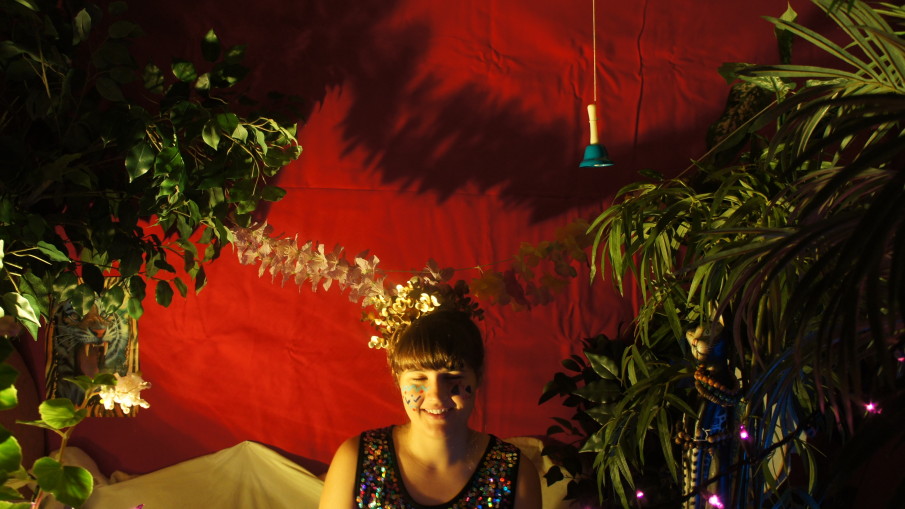 Alexa Dexa wears a sequin dress amidst plants in low lighting.