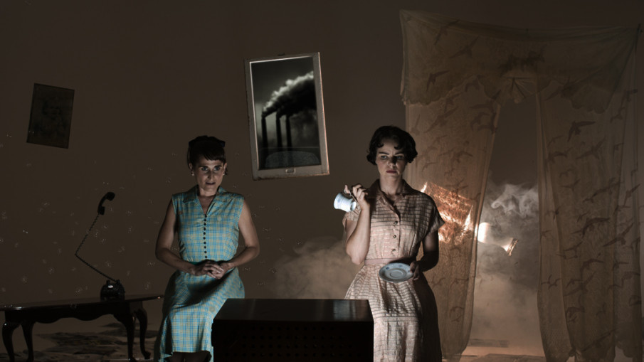 Someone's Trying to Kill Me promo image: Two women in vintage dresses stand before a television.