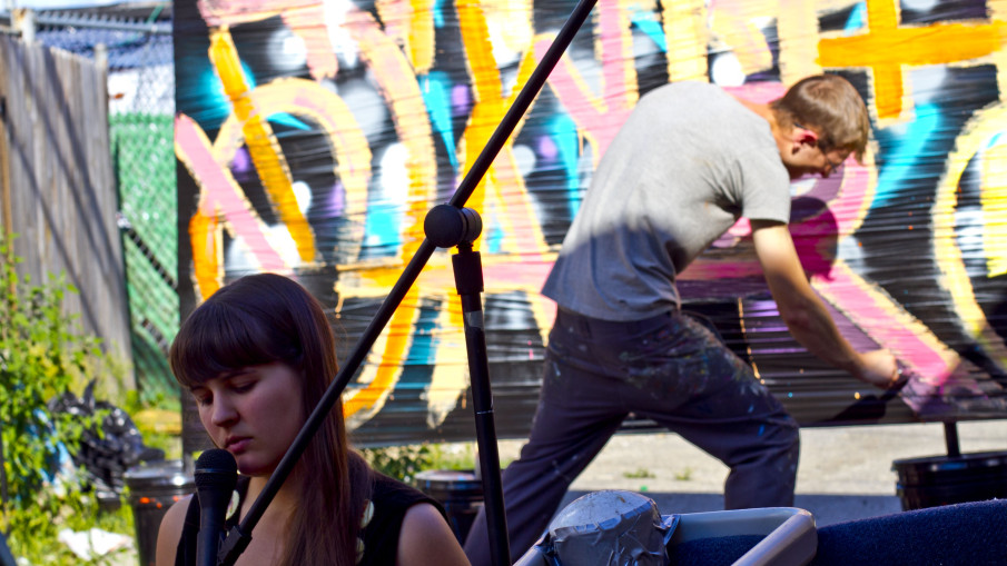 Alexa Dexa plays a live show outside in Detroit while artist Kevin McCoy live paints the words "handle with care" behind them.