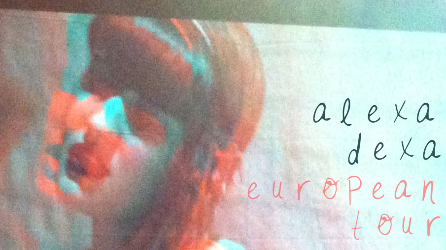 A projection of Alexa Dexa singing in a room with hanging fairy lights and text that reads "alexa dexa european tour".